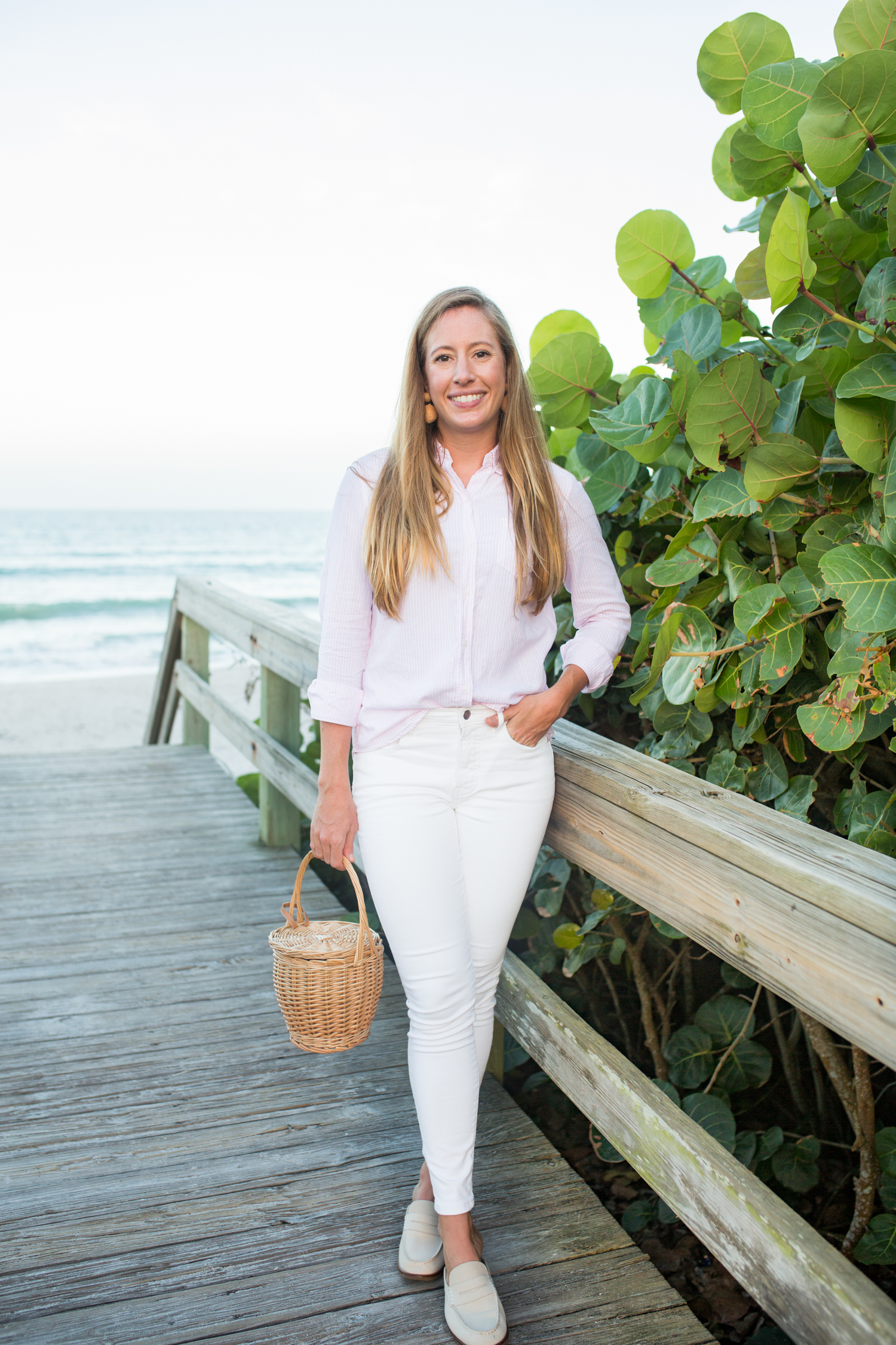 Woman at the beach wearing pink button down top and white jeans as timeless wardrobe essentials. 