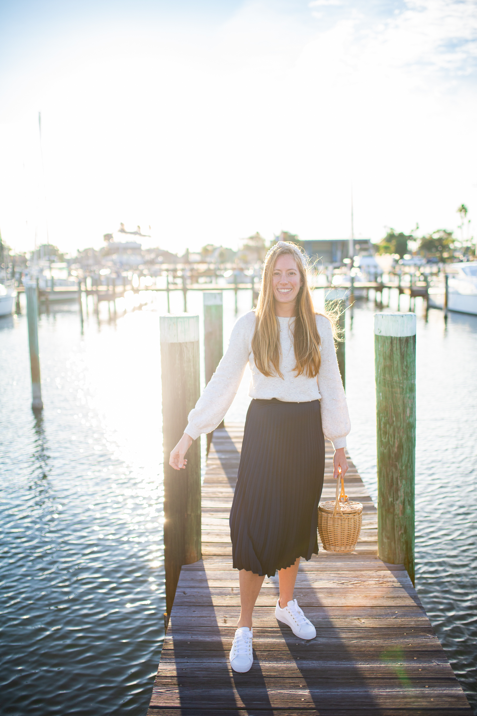 woman wearing white Sweaters for Spring, blue, skirt, and white sneakers at the docks in sunshine, florida at sunset