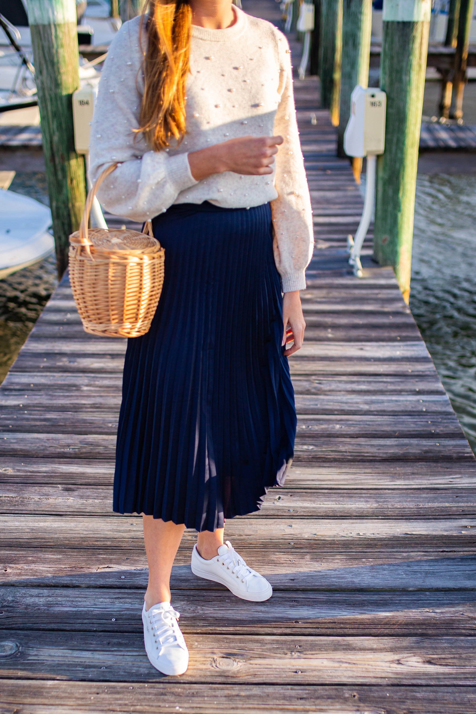 closeup phot of woman wearing white Sweaters for Spring, blue, skirt, and white sneakers at the docks in sunshine, florida