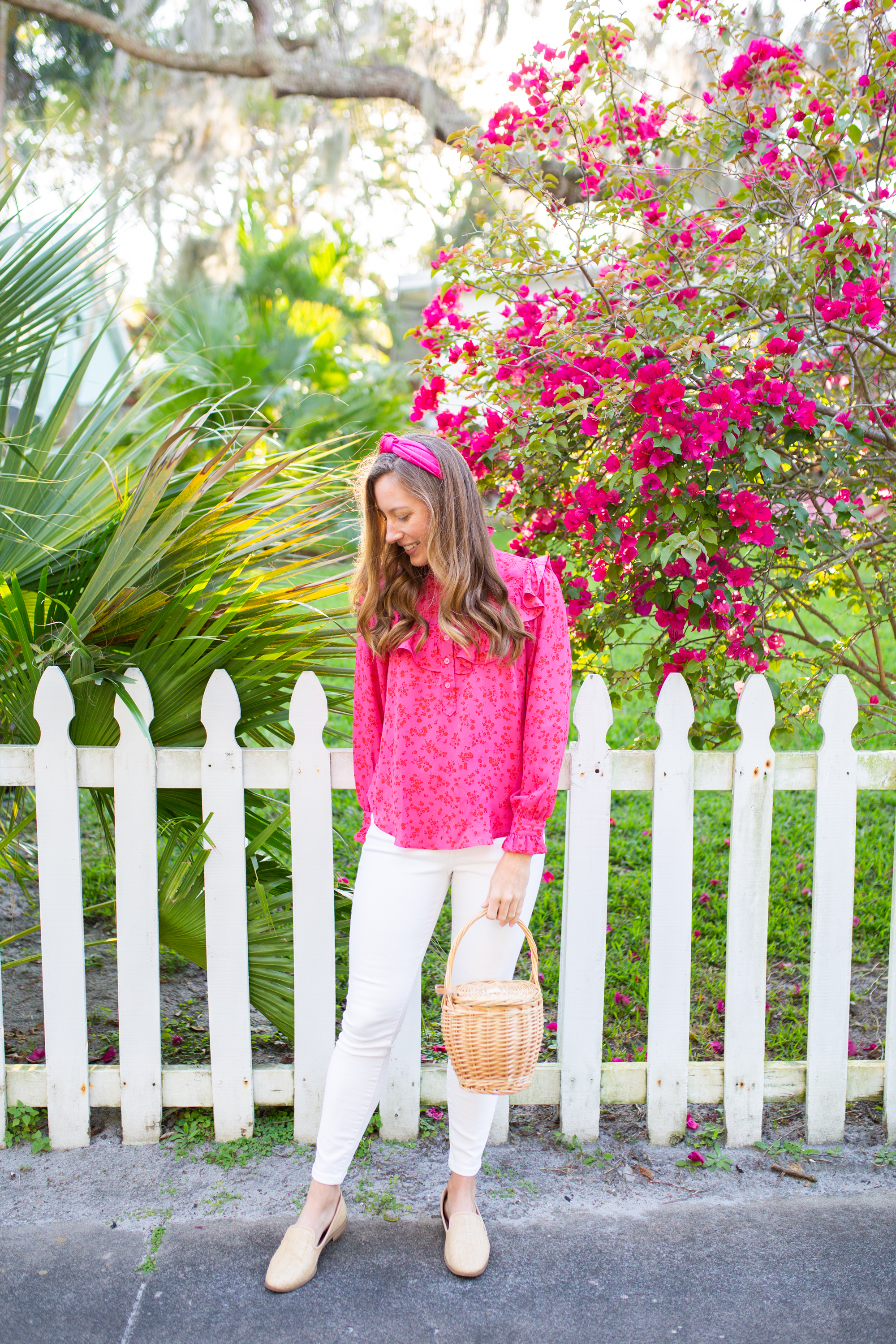 woman wearing Floral Tops for Spring with Ruffle, White Jeans, pink headband, nude flats, and holding a weaved bag