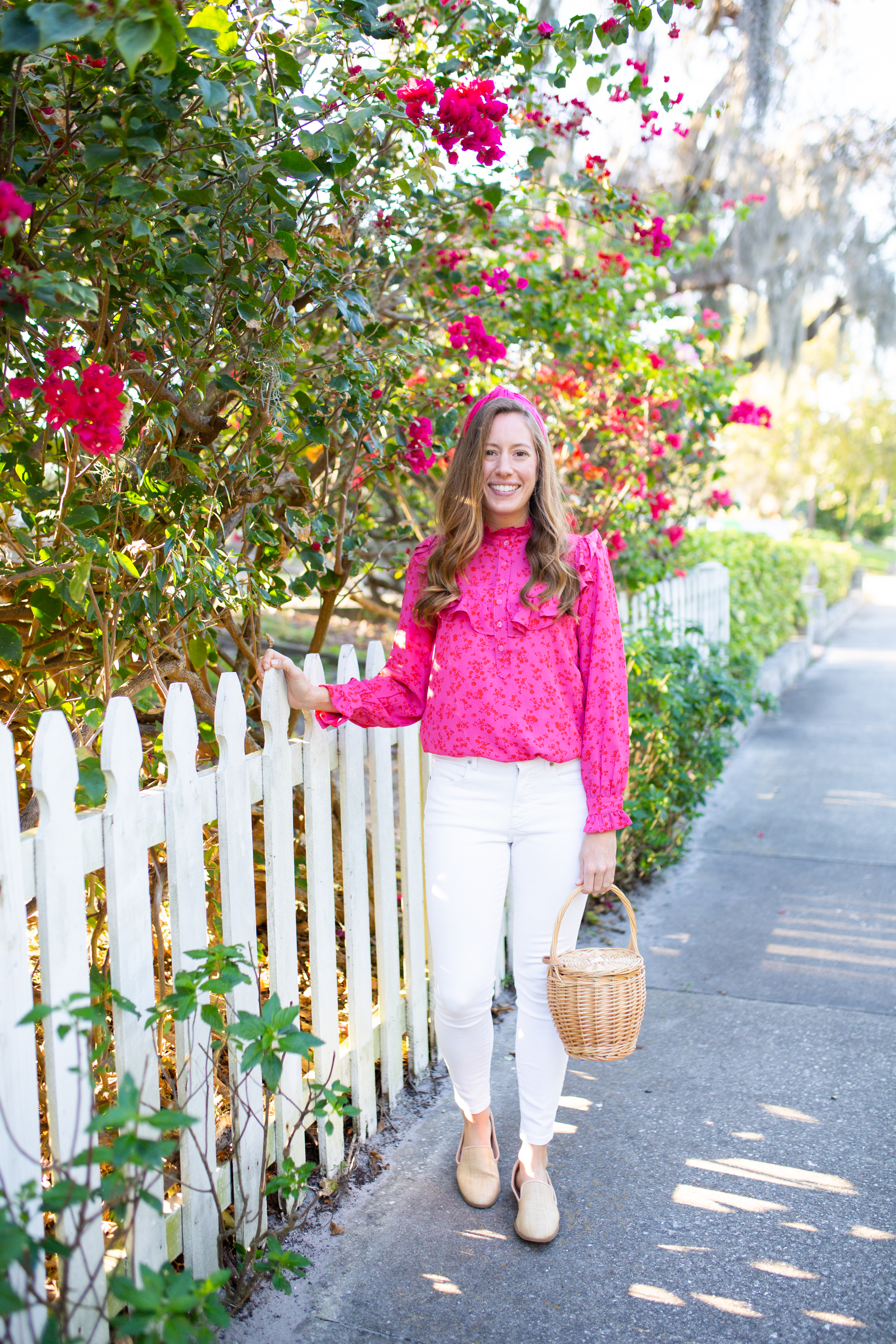 woman wearing Floral Tops for Spring with Ruffle, White Jeans, pink headband, nude flats, and holding a weaved bag