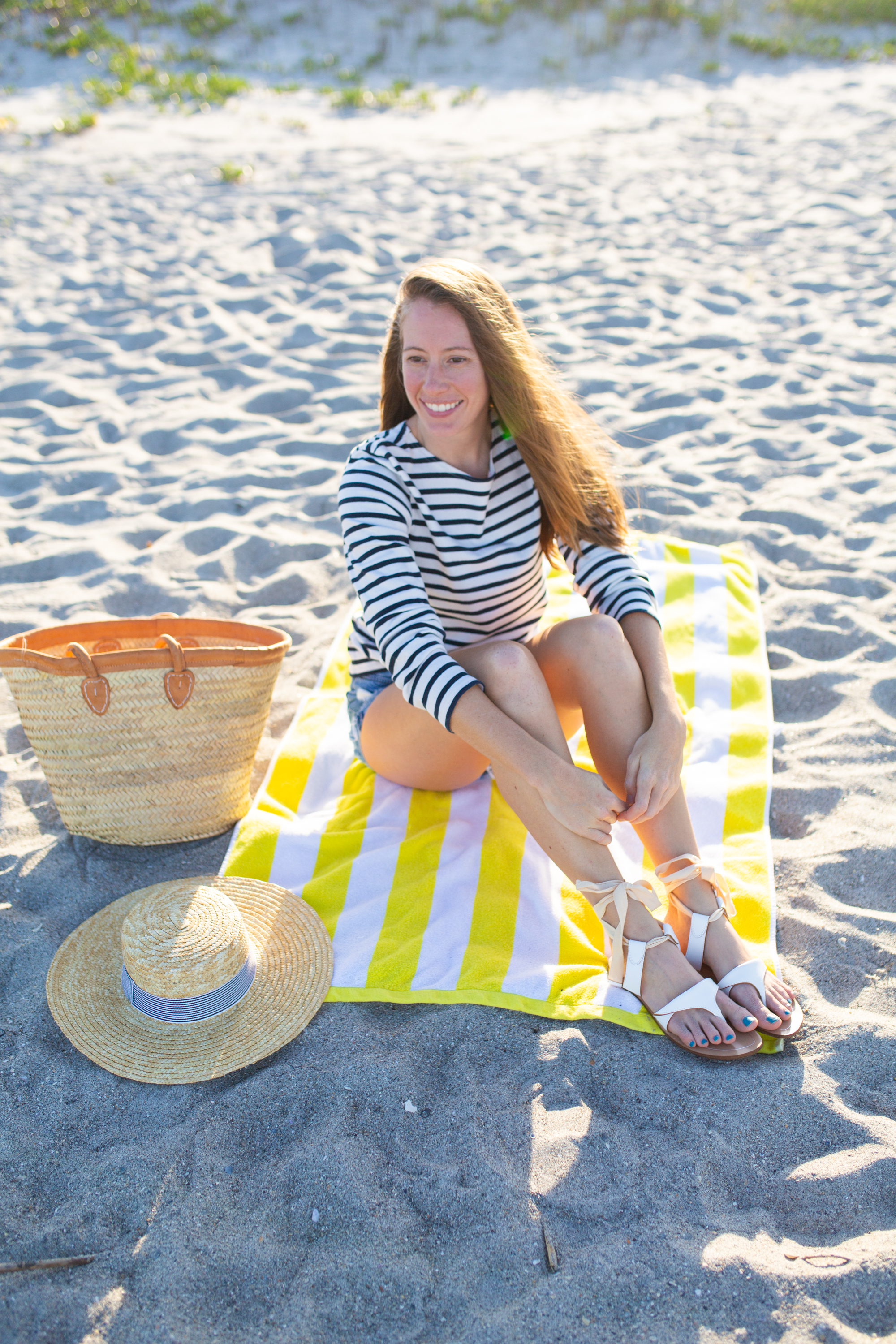 woman sitting at the beach and sitting at a beach towel with bag and hat