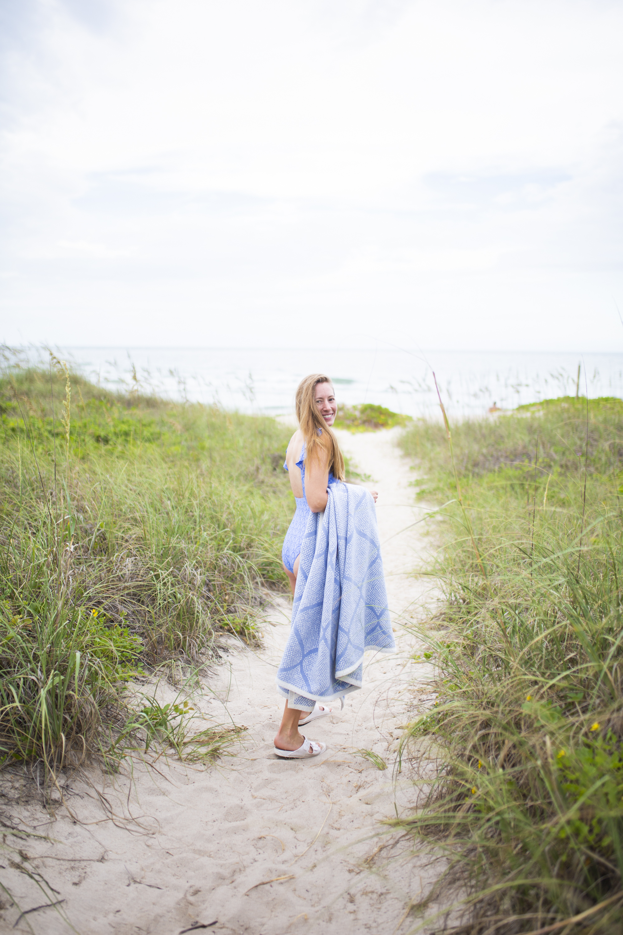 girl walking on the beach with a Chappywrap Blanket and Summersalt swimsuit 