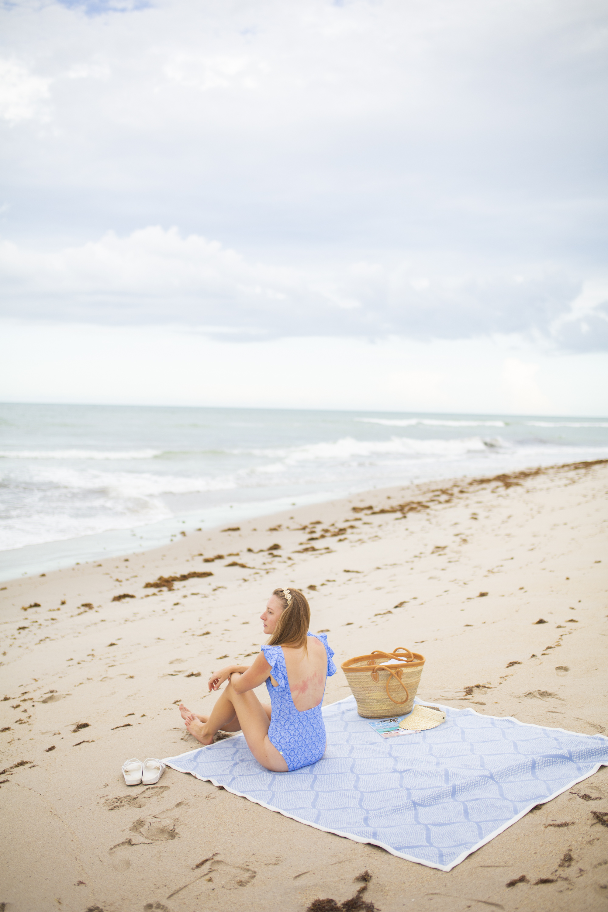 women sitting on beach towel with beach bag overlooking the ocean 