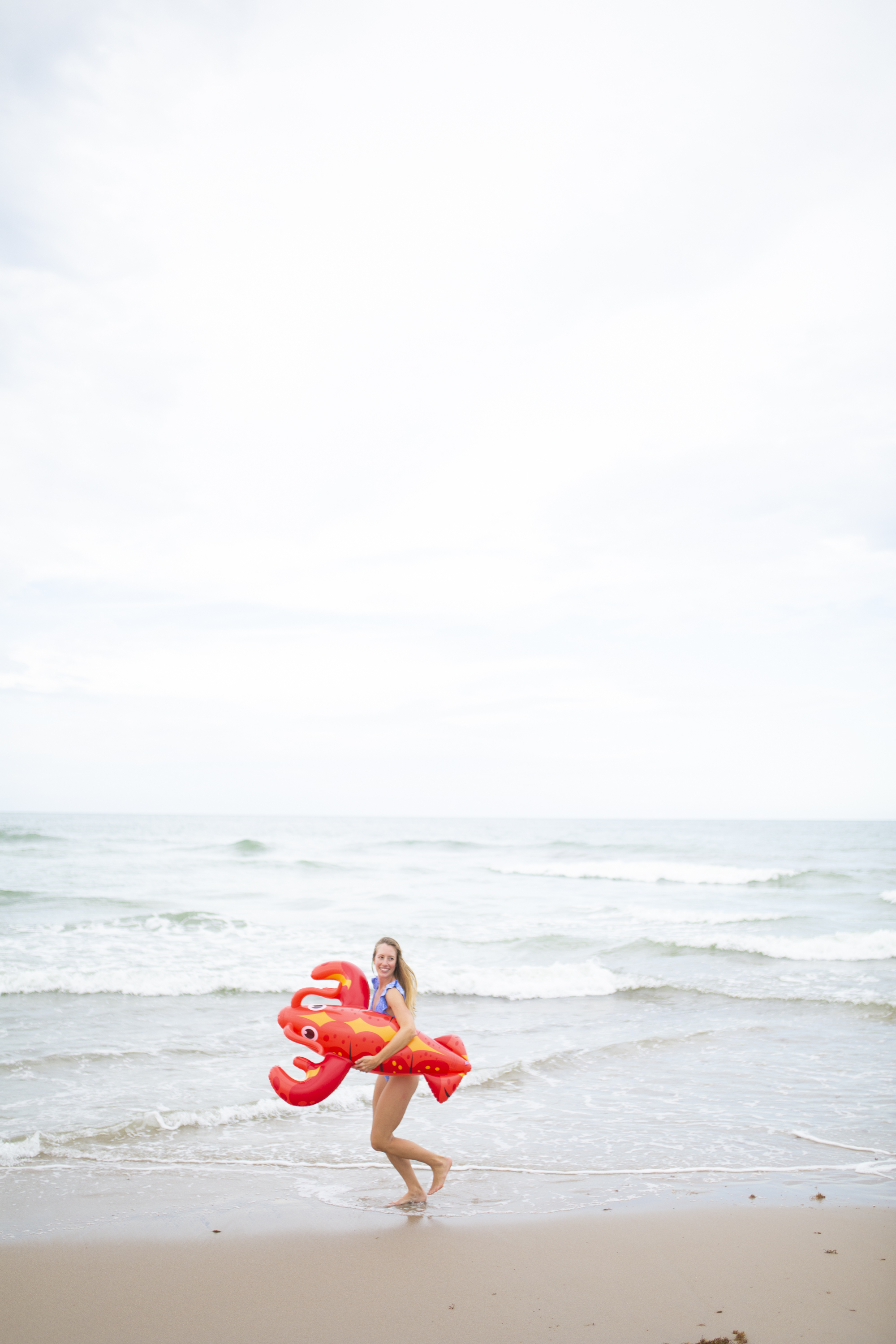 girl running on the beach with a lobster float wearing a blue and white swimsuit 